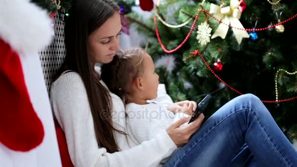 Mladá matka a dcera pomocí smartphone v interiéru vánoční zdobené — Stock video