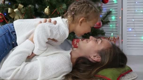 Słodkie dziewczyny trochę zabawy i całując jej mama obok choinki — Wideo stockowe