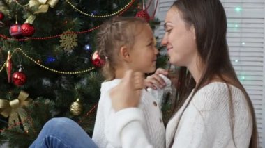 Sevimli küçük kız eğleniyor ve annesi Noel ağacının yanındaki öpüşme
