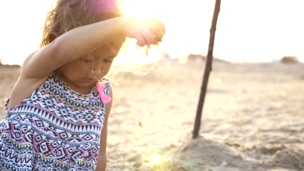 Niña sosteniendo arena en la mano en una playa y dejándola caer de nuevo . — Vídeos de Stock