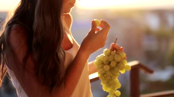 Giovane donna che tiene un grappolo d'uva e li mangia sul balcone, primo piano — Video Stock