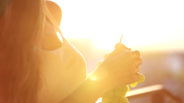Mladá žena držící spoustu hroznů a jíst je na balkoně, detail — Stock video