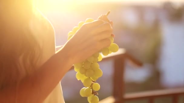 Junge Frau hält eine Traube in der Hand und isst sie auf dem Balkon, Nahaufnahme — Stockvideo