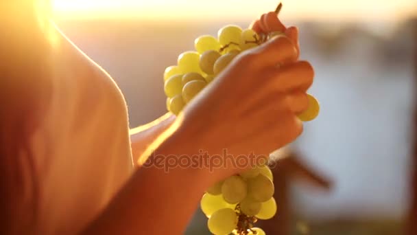 Jeune femme tenant un bouquet de raisin et les mangeant sur le balcon, gros plan — Video