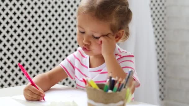 Linda niña preescolar sentada junto a la mesa blanca se centró en dibujar algo . — Vídeo de stock