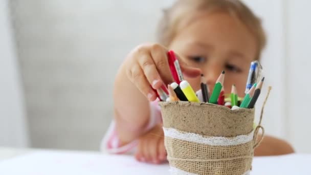 Menina pré-escolar bonito sentado ao lado da mesa branca focada em desenhar algo . — Vídeo de Stock