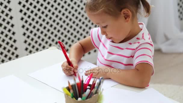 Jolie fille préscolaire assise à côté de la table blanche axée sur le dessin quelque chose . — Video