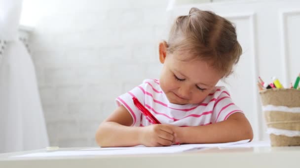 Linda niña preescolar sentada junto a la mesa blanca se centró en dibujar algo . — Vídeos de Stock