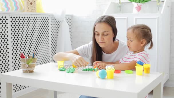 Mutter mit süßer kleiner Tochter spielt mit Modelliermasse im hellen Wohnzimmer. — Stockvideo