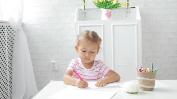 Jolie fille préscolaire assise à côté de la table blanche axée sur le dessin quelque chose . — Video