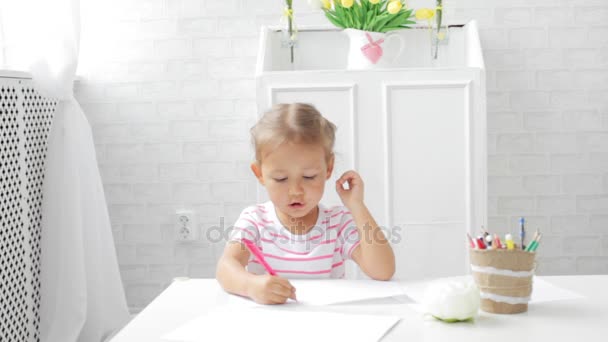 Nettes Vorschulmädchen sitzt am weißen Tisch und konzentriert sich darauf, etwas zu zeichnen. — Stockvideo