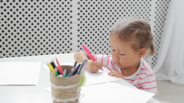 Schattig preschool meisje zit door de witte tabel gericht op tekening iets. — Stockvideo