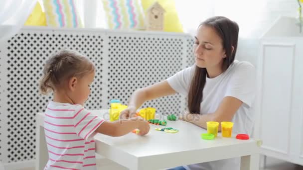 Mutter mit süßer kleiner Tochter spielt mit Modelliermasse im hellen Wohnzimmer. — Stockvideo