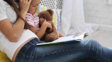 Genç anne küçük kızı için kitap okumak.