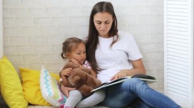 Genç anne küçük kızı için kitap okumak.