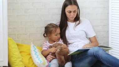 Genç anne küçük kızı için kitap okumak.