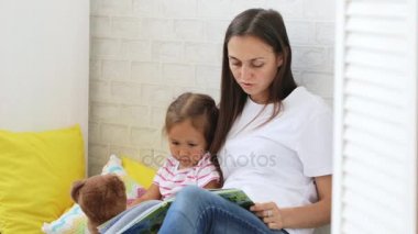 Genç anne küçük kızı için kitap okumak.