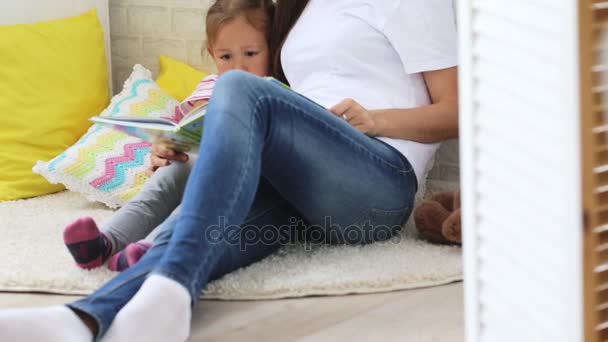 Jonge moeder leesboek voor haar dochtertje. — Stockvideo