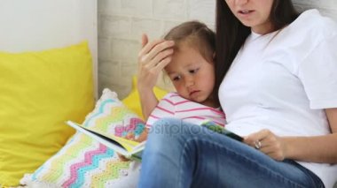 Genç anne küçük kızı için kitap okumak.