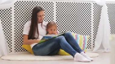 Genç anne küçük kızı için kitap okumak.