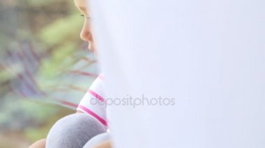 Ellerin diz pencere kenarında oturan sevimli küçük kız, yakın çekim.