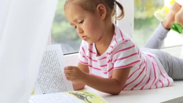 Εσωτερικη πορτρέτο του ανάγνωση του βιβλίου σε windowsill στο σπίτι το μικρό χαριτωμένο κορίτσι. — Αρχείο Βίντεο