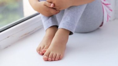 Ellerin diz pencere kenarında oturan sevimli küçük kız, yakın çekim.