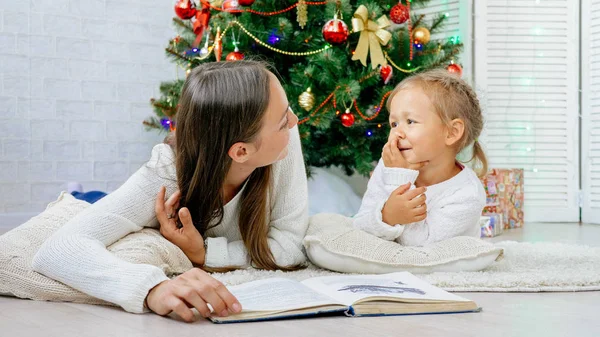 Mother and cute little dautgher lying on the floor and reading book at xmas eve. Royalty Free Stock Photos