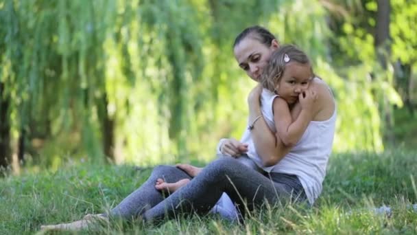 Мать и дочь сидят и обнимаются во время занятий йогой в зеленом парке — стоковое видео