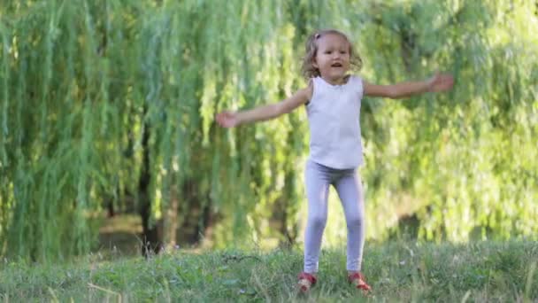 Petite fille mignonne et sportive faisant des exercices de cric sautant sur la prairie dans le parc . — Video