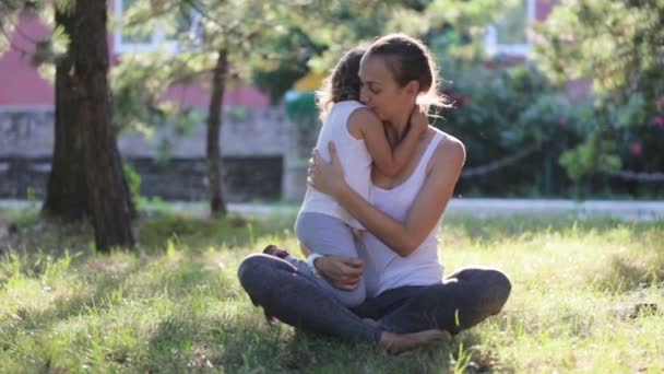 Mother and daughter sitting and embracing when doing yoga exercise in green park — Stock Video