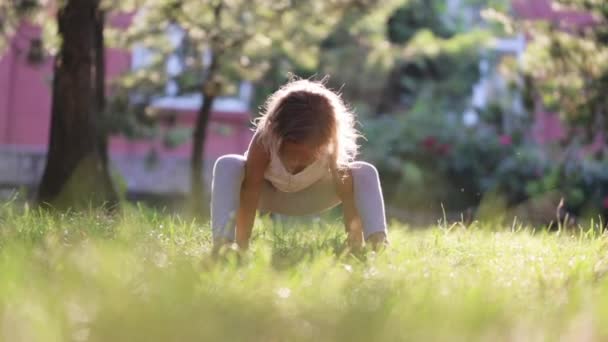 Kleines süßes Baby-Mädchen macht Yoga-Übungen auf dem Rasen im Park. — Stockvideo