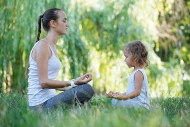 Genç anne ve sevimli küçük kız meditasyon lotus birlikte poz