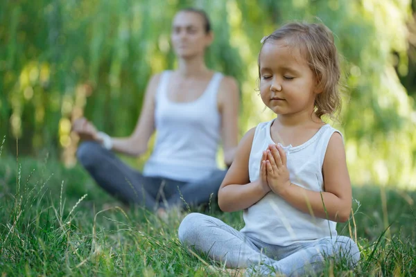Genç anne ve sevimli küçük kız meditasyon lotus birlikte poz