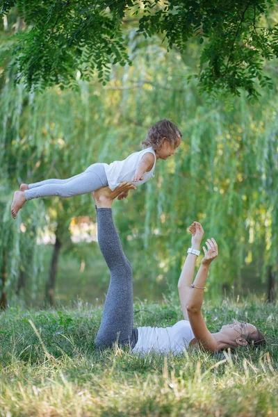 Anya és lánya jógáznak a parkban a füvön napközben.. — Stock Fotó