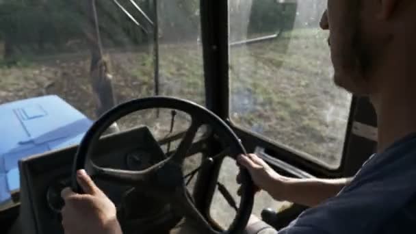 Farmer in hat, sits inside in the tractor cabin, rides on the field with plow. — Stock Video