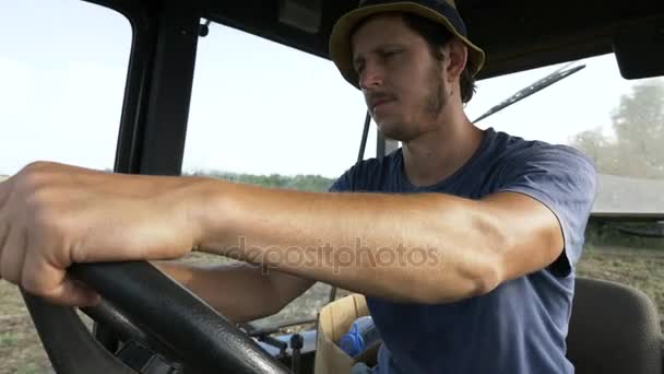 Fermier en chapeau, assis à l'intérieur dans la cabine du tracteur, promenades sur le terrain avec charrue . — Video