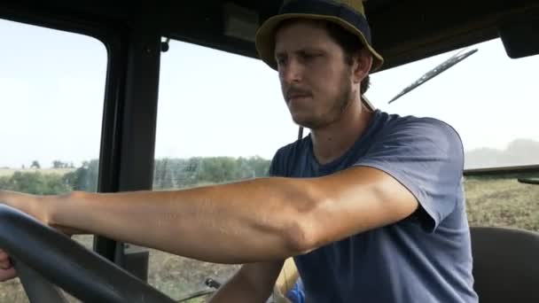 Fermier en chapeau, assis à l'intérieur dans la cabine du tracteur, promenades sur le terrain avec charrue . — Video