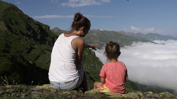 Mujer joven con una linda hija sentada en la cima de la montaña . — Vídeos de Stock