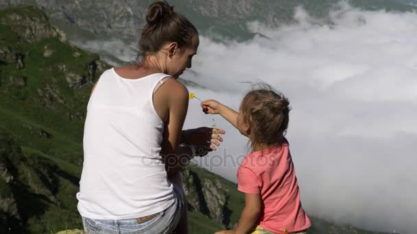 Jonge vrouw met kleine schattige dochter zit op de top van de berg. — Stockvideo