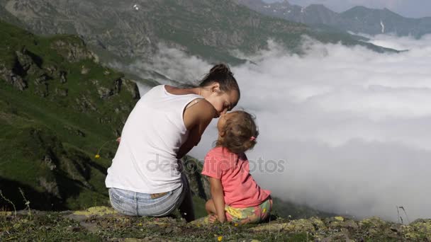 Mujer joven con una linda hija sentada en la cima de la montaña . — Vídeo de stock