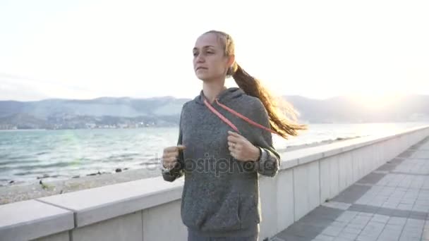 Mujer joven vestida con sudadera con capucha corriendo en la ciudad en primera línea de mar — Vídeo de stock