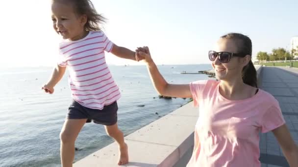 Joven madre con hija pequeña corriendo cogida de la mano, sonriendo y riendo — Vídeo de stock