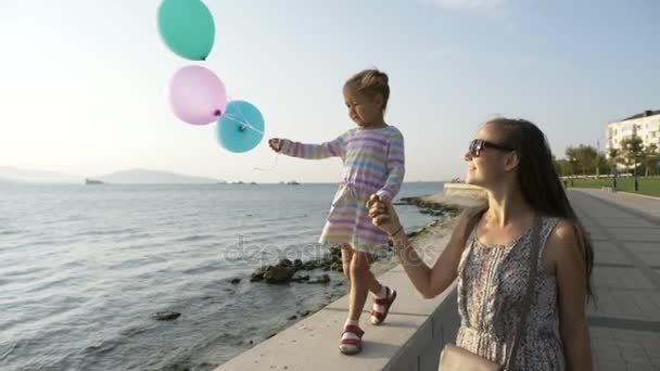 Kvinna går hand med en liten vacker flicka på morgon i staden vid havet — Stockvideo