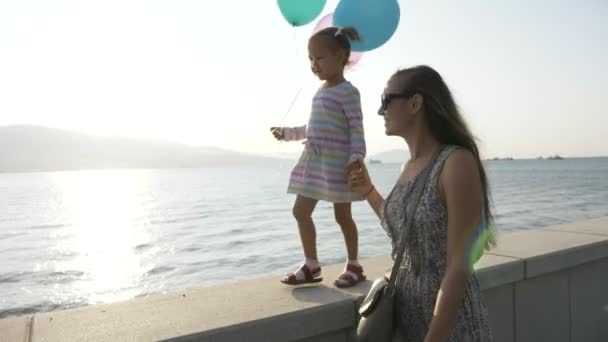 Женщина идет за руку с маленькой красивой девочкой утром на побережье города — стоковое видео