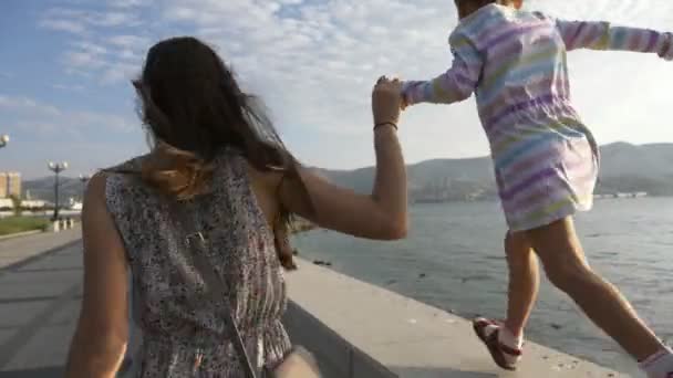 Kvinnan kör i handen med en liten vacker flicka på morgon i staden vid havet — Stockvideo