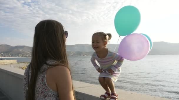 Petite fille mignonne sautant du trottoir aux mains sa jeune mère au bord de la mer — Video