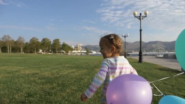Cute little girl running with balloons in the park and laughing — Stock Video
