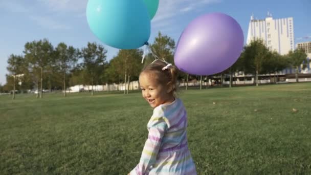 Милая маленькая девочка бегает с воздушными шарами в парке и смеется — стоковое видео