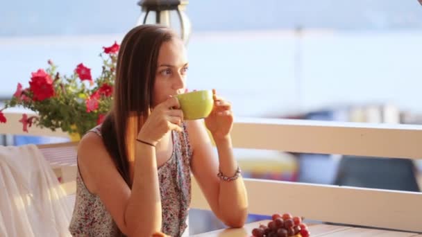 Young pretty woman sits in a cafe beholding beautiful views of sea bay. — Stock Video